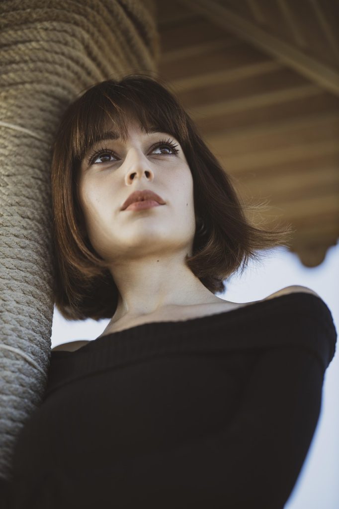 Person leaning against a rope-wrapped column, gazing upward, wearing an off-shoulder black top