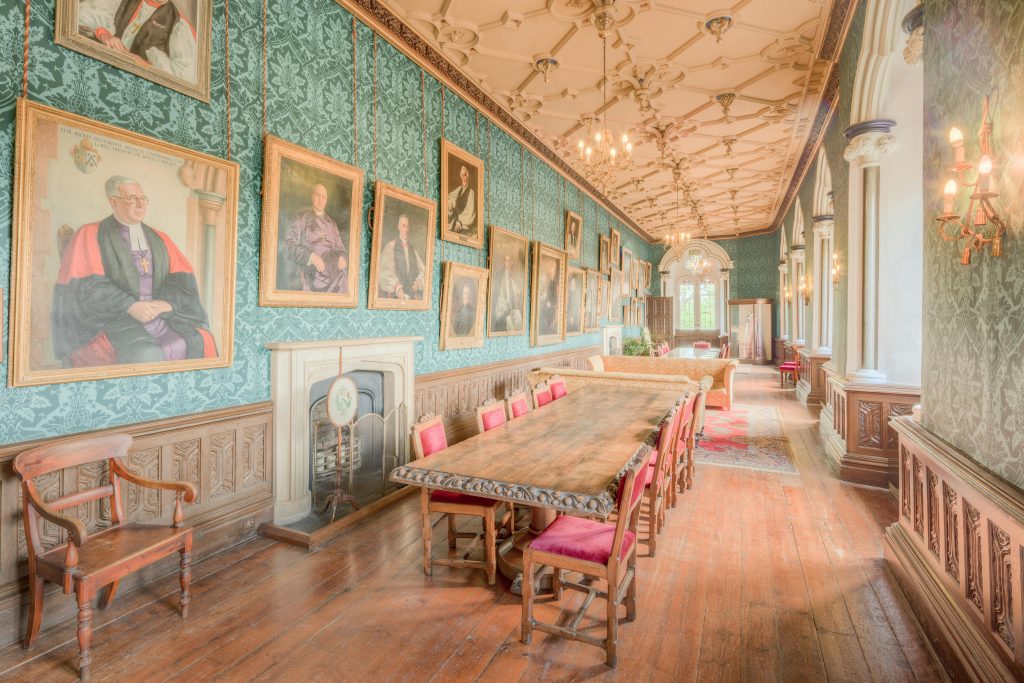 Historic corridor in England with ornate decor and framed portraits, showcasing classic British interior design.