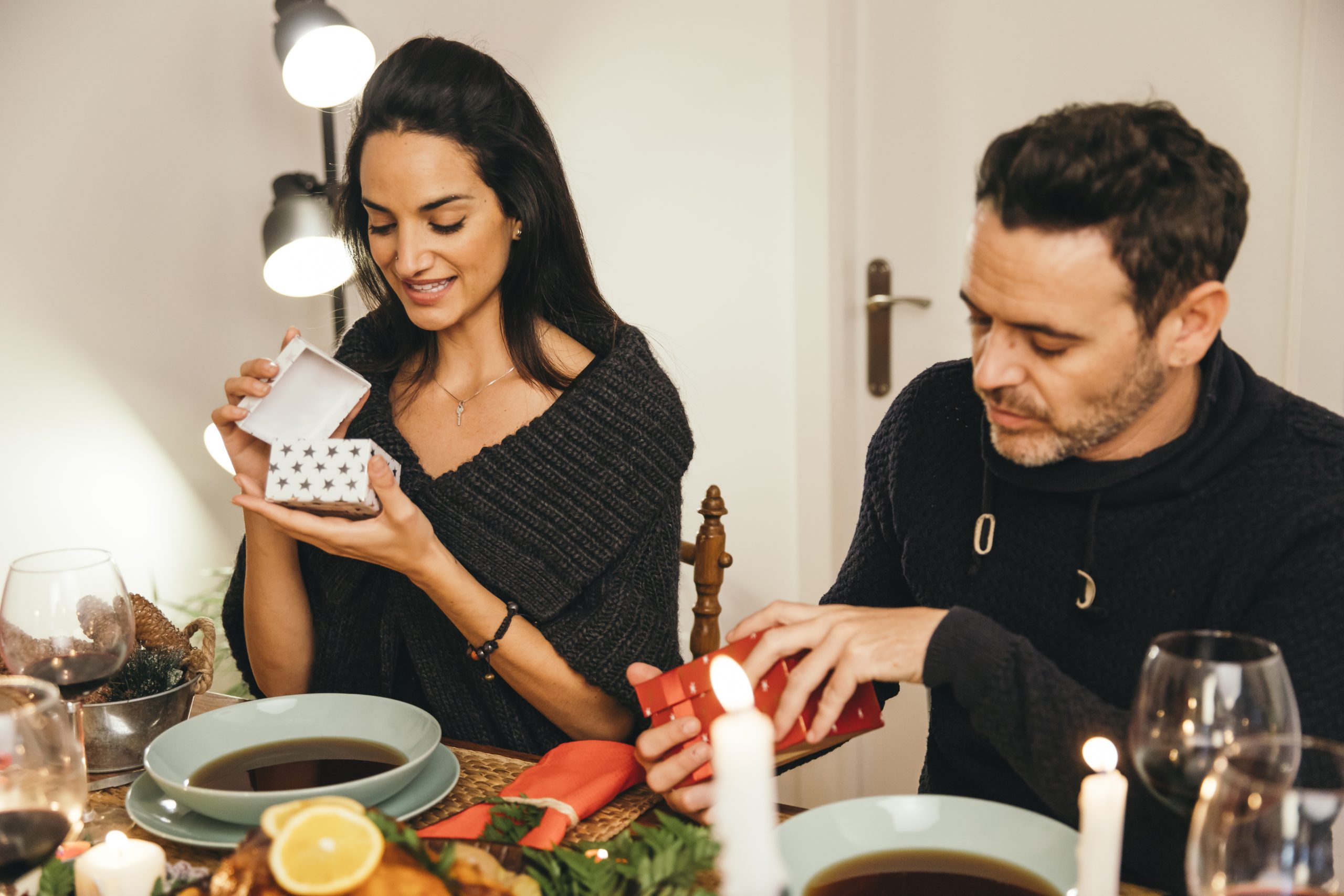 Couple exchanging gifts at festive dinner table with candles and wine glasses